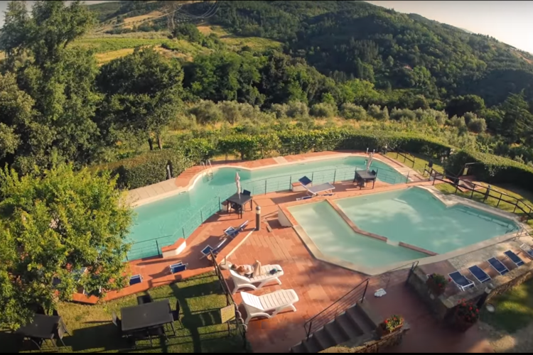 View from above of the two pools surrounded by the green of the hillside on which Borgo La Casaccia sits